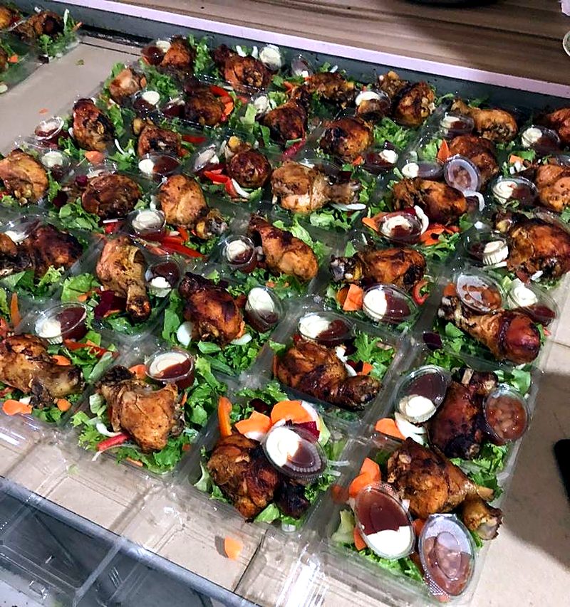 Grilled chicken on fresh salad in clear containers, with sauce and mayonnaise cups.