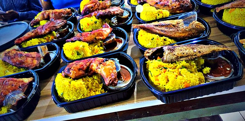 Packed meals of turmeric rice with grilled chicken and fried fish, laid out on a table.